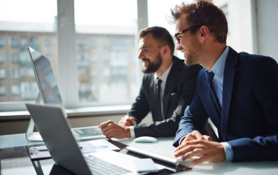 Smiling businessman and his colleague looking at computer monitor at meeting